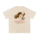 A beige short-sleeve t-shirt with a brown graphic of a woman holding a coffee cup and the text 'MONACO'S coffee co.' printed on the front, shown against a plain white background.