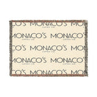 A rectangular woven throw blanket with fringed edges, featuring a cream background with a repeating dark gray 'MONACO'S MOON coffee co.' logo pattern and multicolor fringe.