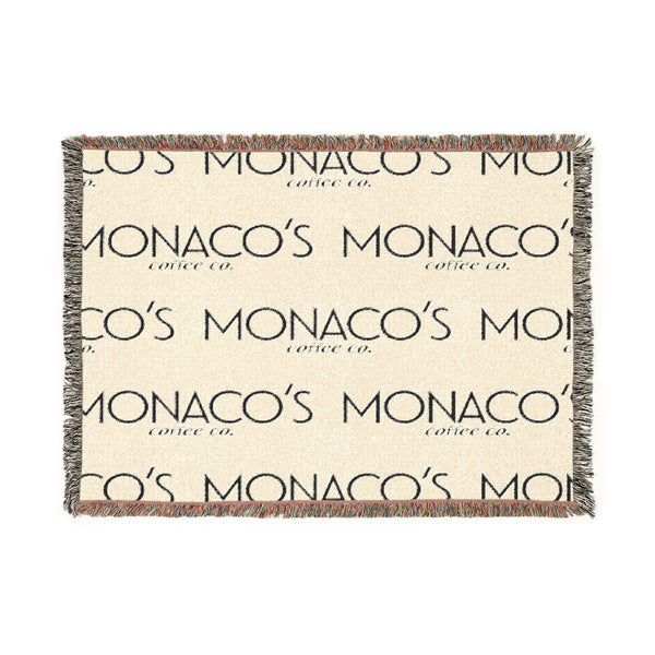A rectangular woven throw blanket with fringed edges, featuring a cream background with a repeating dark gray 'MONACO'S MOON coffee co.' logo pattern and multicolor fringe.