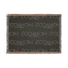 A rectangular woven scarf with fringe on all sides, featuring the brand name 'Monaco' woven repeatedly in light beige on a dark charcoal gray background.